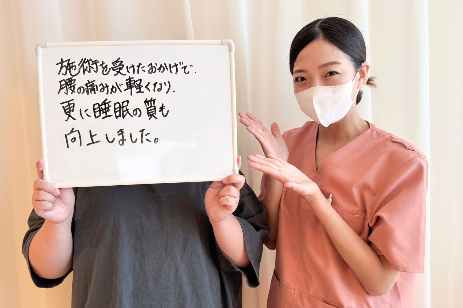 「施術を受けたおかげで、腰の痛みが軽くなり、更に睡眠の質も向上しました。」と書かれたホワイトボードを持つ患者さまと担当鍼灸師