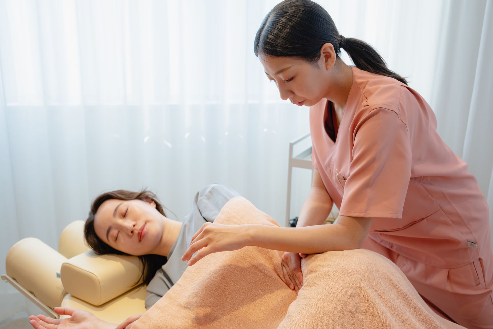 横向きに寝た患者さまの背中に、女性鍼灸師が手を当てて施術している様子