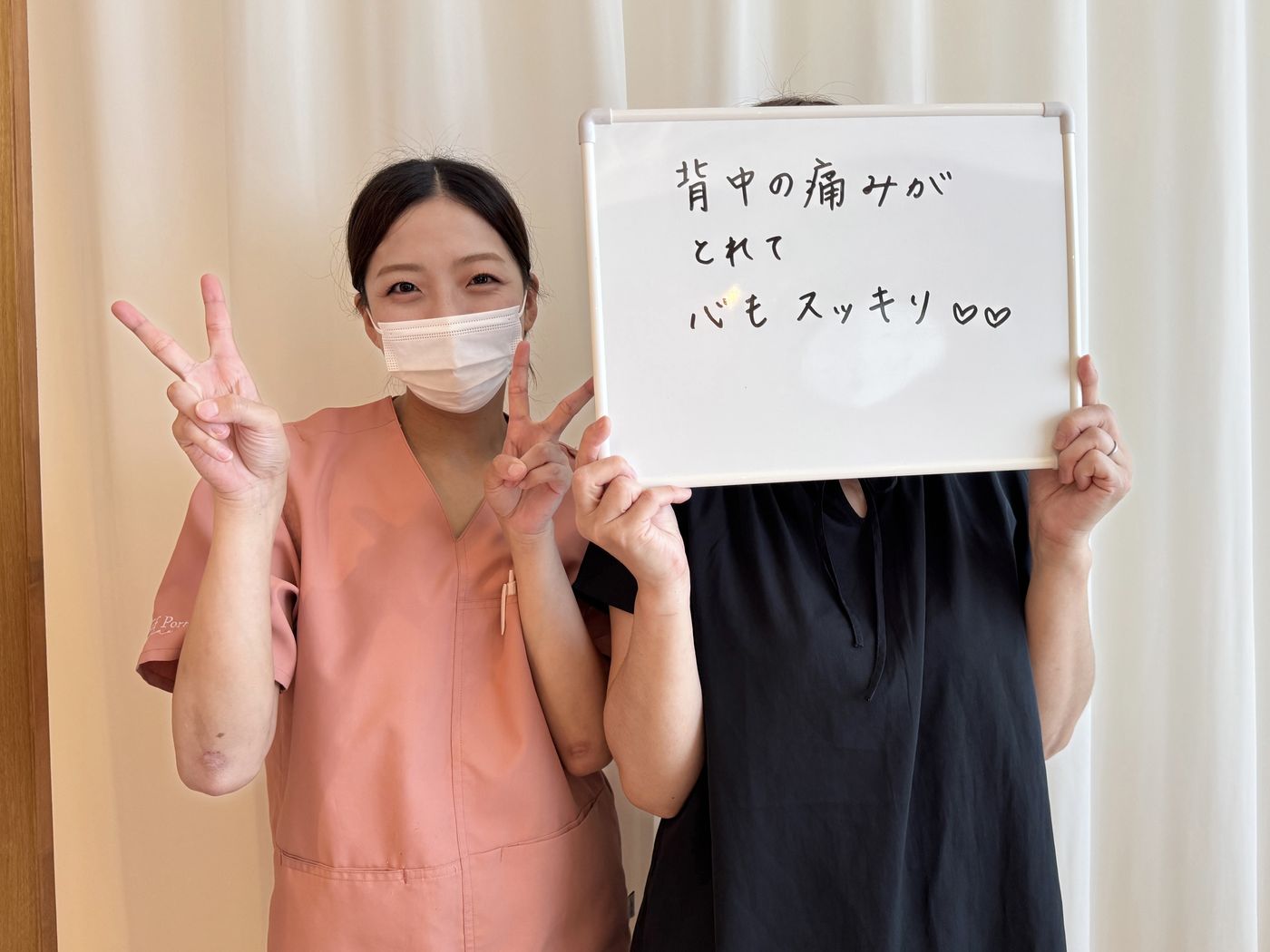「背中の痛みがとれて心もスッキリ」と書かれたホワイトボードを持つ患者さまと鍼灸師