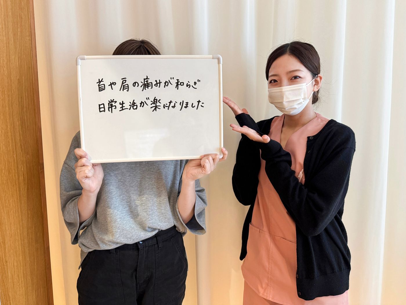 「首や肩の痛みが和らぎ日常生活が楽になりました」と書かれたホワイトボードを持つ患者さまと鍼灸師